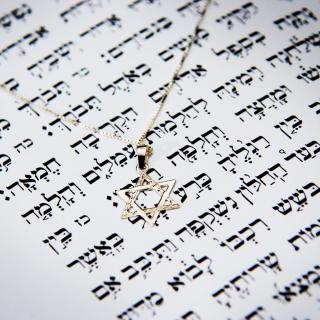 Eine Kette mit einem silbernen Davidstern-Anhänger liegt auf einer Textseite in hebräischer Schrift.