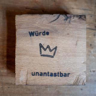 Eine sogenannte "Würdetafel" ist ein Holzquadrat mit einer Krone und der Aufschrift "Würde unantastbar".