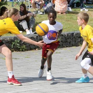 Zwei Jungen und ein Mädchen spielen Streetbasketball.