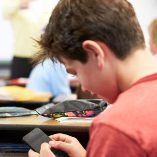 Ein Schüler sitzt im Unterricht und blickt auf das Handy in seiner Hand.