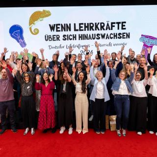 Das Gruppenbild zeigt die Preisträgerinnen und Preisträges des Deutschen Lehrkräftepreises. Sie halten die Hände hoch. 