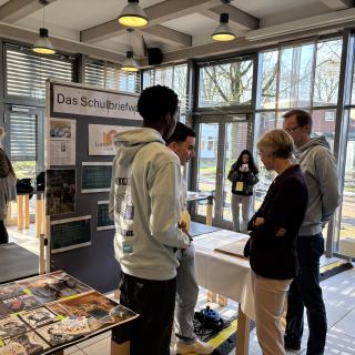 Schulministerin Feller steht mit Schülerinnen und Schülern vor einem Stand der Regionalen Lernstatt NRW über die Schulbriefwahl.