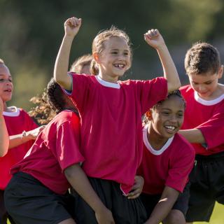 Kinder in Sport-Trikots stehen jubelnd zusammen.