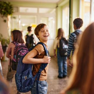 Symbolbild: Mehrere Kinder in einem Schulflur, ein Schüler schaut lächelnd zurück.