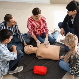 Lehrkräfte, Schülerinnen und Schüler üben die Reanimation an einem Wiederbelebungsphantom.