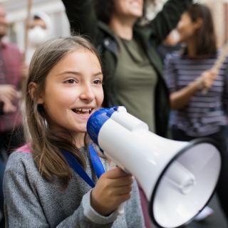 Symbolbild: Mädchen mit einem Megafon in einer Gruppe Demonstrierender.