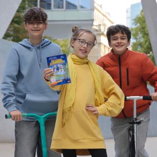 Drei Jugendliche halten das aktuelle Buch der Buch-Gutschein-Aktion 2026 in der Hand.