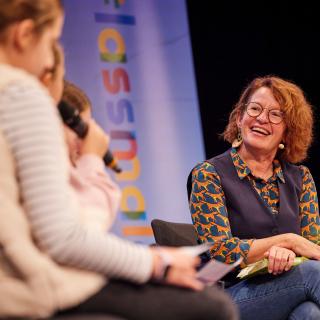 Bei einer Lesung sitzen Schülerinnen mit auf dem Podium und stellen Fragen.