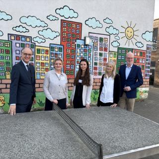 An der Südparkschule Gladbeck stehen Sts Dr. Mauer, Schulleiterin Viola Beyer, Laura Theben (erweiterte Schulleitung, Klassenlehrerin), Natascha Stahl von der Schulaufsicht Recklinghausen, Martin Teuber, Referatsleiter 33 im MSB an einer Tischtennisplatte.