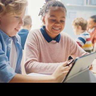 Ein Junge und ein Mädchen sitzen gemeinsam an einem Tablet.