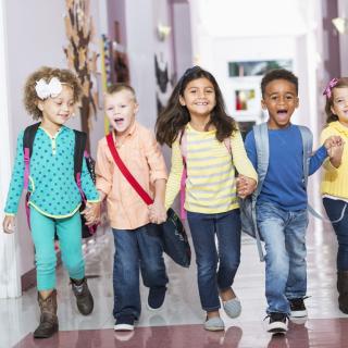 Vorschulkinder laufen Hand in Hand durch einen Schulflur.