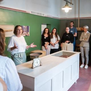 Ministerin Feller sowie Lehramtsanwärterinnen und -anwärter stehen in einem Raum des Humberghauses und hören einer Führung zu.