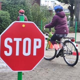 Ein Kind fährt Fahrrad, im Vordergrund steht ein Stop-Schild