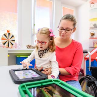 Lehrerin und Kind nutzen ein Gerät der unterstützten Kommunikation.