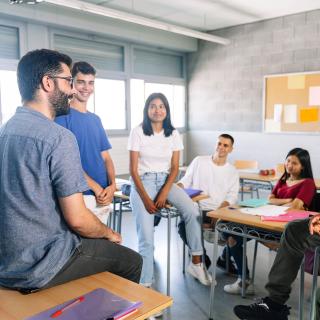 Schülerinnen und Schüler diskutieren mit einem Lehrer.