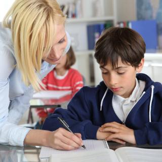 Eine Lehrerin beugt sich im Unterricht helfend über einen Schüler.