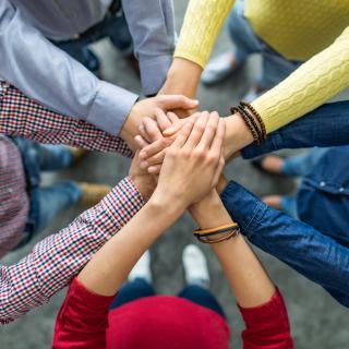 Fünf Menschen stehen im Kreis und legen ihre Hände aufeinander, die Gesichter sind nicht zu erkennen.