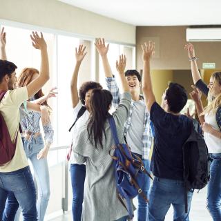 Eine Gruppe Schüler steht in einem Schulflur und hat die Hände zum "High Five" erhoben.