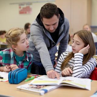 Ein Lehrer mit Migrationshintergrund in einer Unterrichtssituation mit zwei Schülerinnen.