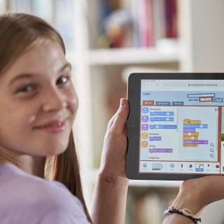 Mädchen zeigt ein Tablet, auf dem das Bildungsangebot des WDR sichtbar ist.