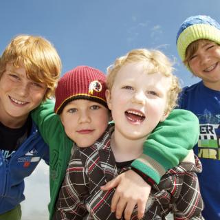 Vier Kinder unterschiedlichen Alters blicken vor blauem Himmel lächelnd in die Kamera