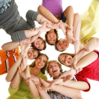 Eine Gruppe Jugendlicher steht mit ineinander verschränkten Armen im Kreis und blickt von oben in die Kamera.